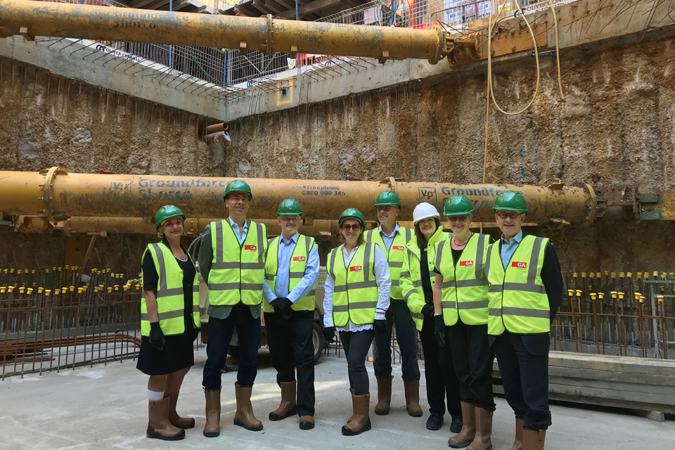 A group of donors, wearing suits under their hi-vis jackets and hard helmets, with pipes behind them, smiling at the camera.